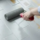 Applicazione di smalto per pavimenti: un rullo stende il grigio su piastrelle, valutando smalto per pavimenti pro e contro per un restyling.