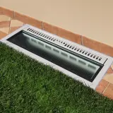 Bocche di lupo moderne con griglia metallica e illuminazione integrata, incassate tra prato verde e pavimentazione in cotto.