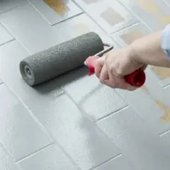 Applicazione di smalto per pavimenti: un rullo stende il grigio su piastrelle, valutando smalto per pavimenti pro e contro per un restyling.