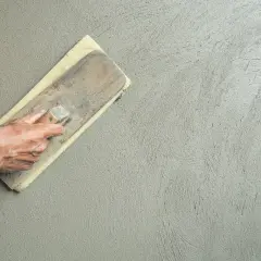 Mano che esegue la rasatura di un muro con frattazzo, creando una finitura liscia e uniforme.