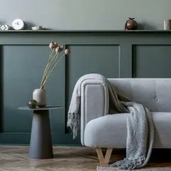 Divano grigio con coperta, vaso con fiori secchi e tavolino su parete con boiserie fai da te.