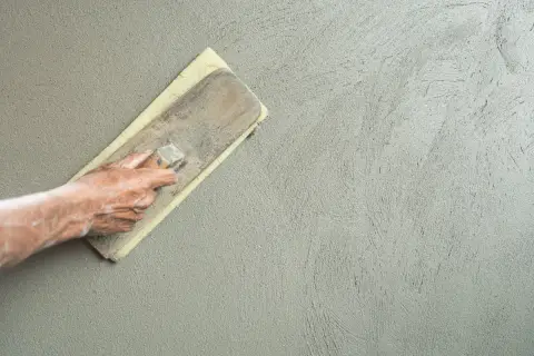 Mano che esegue la rasatura di un muro con frattazzo, creando una finitura liscia e uniforme.