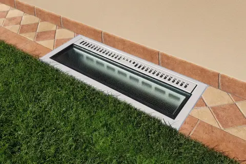 Bocche di lupo moderne con griglia metallica e illuminazione integrata, incassate tra prato verde e pavimentazione in cotto.