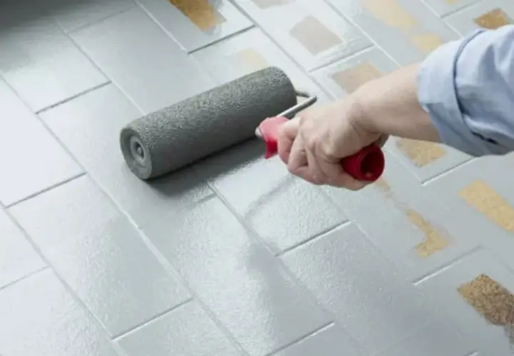 Applicazione di smalto per pavimenti: un rullo stende il grigio su piastrelle, valutando smalto per pavimenti pro e contro per un restyling.