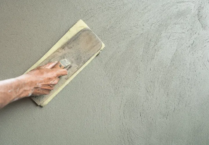 Mano che esegue la rasatura di un muro con frattazzo, creando una finitura liscia e uniforme.