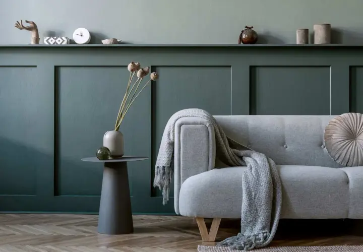 Divano grigio con coperta, vaso con fiori secchi e tavolino su parete con boiserie fai da te.