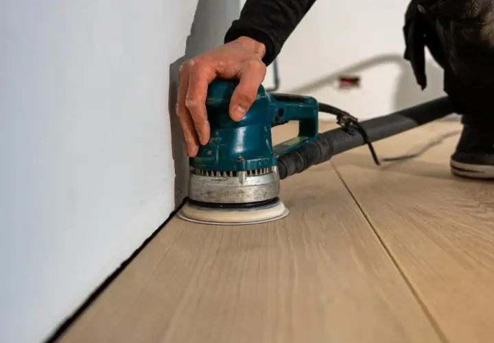 Mano che usa una levigatrice per levigare il parquet, rendendolo liscio e pronto per la finitura.