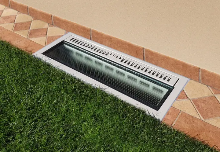 Bocche di lupo moderne con griglia metallica e illuminazione integrata, incassate tra prato verde e pavimentazione in cotto.