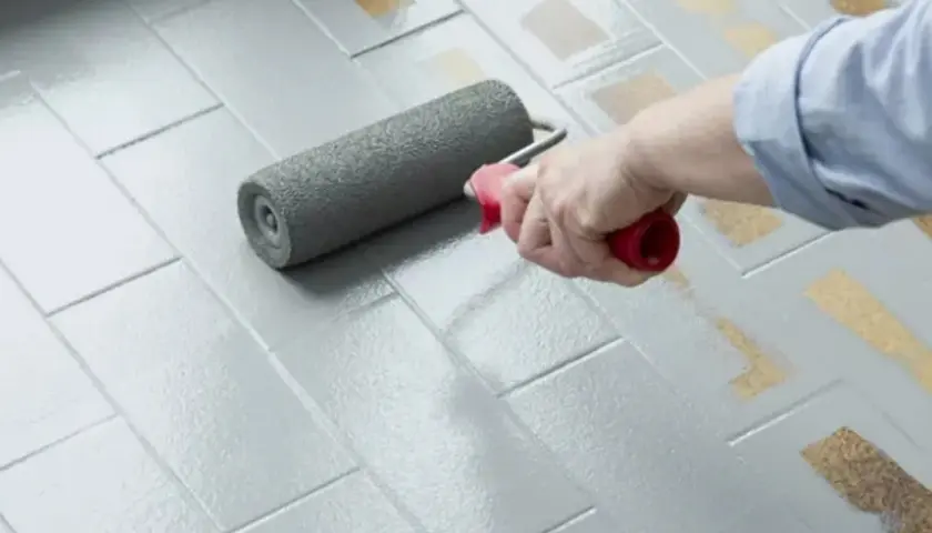 Applicazione di smalto per pavimenti: un rullo stende il grigio su piastrelle, valutando smalto per pavimenti pro e contro per un restyling.