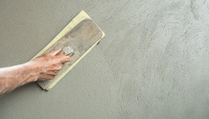 Mano che esegue la rasatura di un muro con frattazzo, creando una finitura liscia e uniforme.
