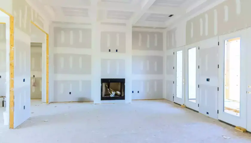 Interno di una stanza in costruzione con pareti in cartongesso insonorizzate, camino e porte a doppio battente.