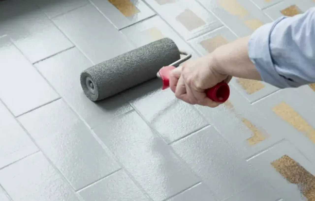 Applicazione di smalto per pavimenti: un rullo stende il grigio su piastrelle, valutando smalto per pavimenti pro e contro per un restyling.