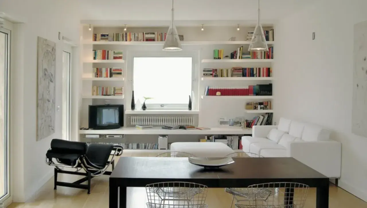 Librerie in cartongesso moderne con libri, TV, divano bianco e tavolo da pranzo.