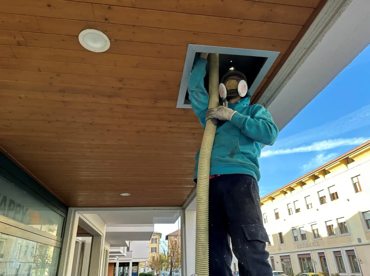 Operaio con maschera e guanti inserisce tubo in un'apertura del controsoffitto isolante termico in legno.