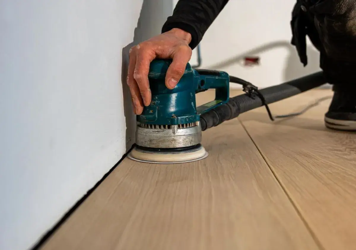 Mano che usa una levigatrice per levigare il parquet, rendendolo liscio e pronto per la finitura.