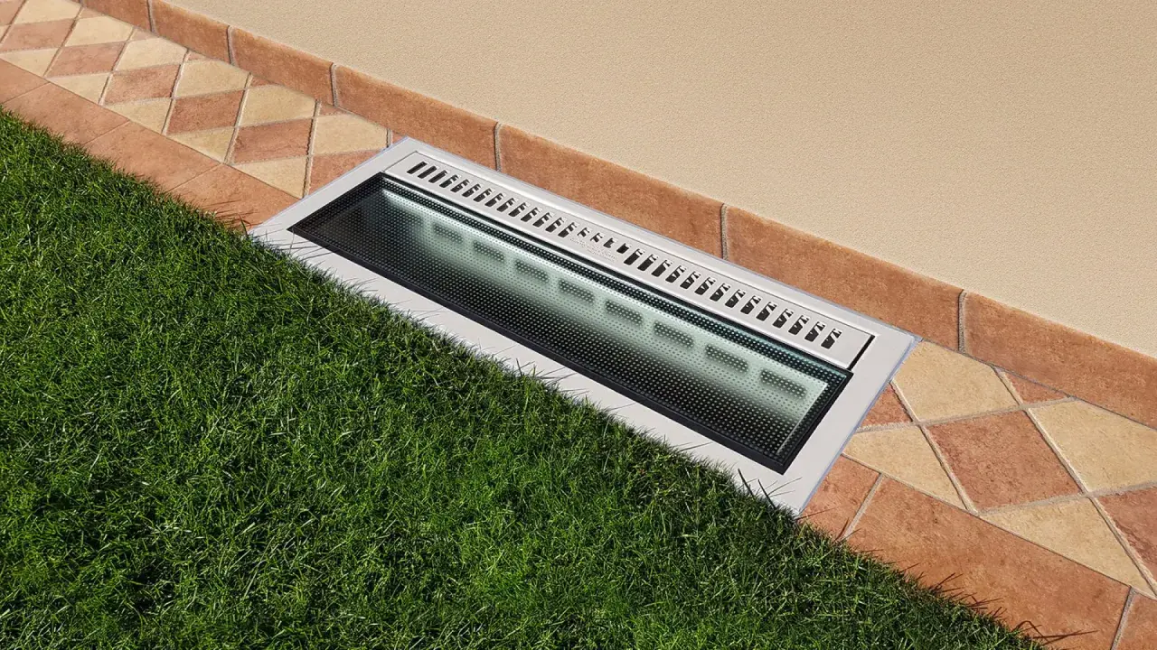 Bocche di lupo moderne con griglia metallica e illuminazione integrata, incassate tra prato verde e pavimentazione in cotto.