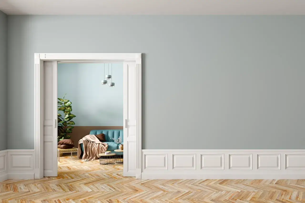 Un elegante soggiorno con divano blu e parquet a spina di pesce. Le pareti sono dipinte in tonalità pastello, con un pannello in cartongesso effetto legno che aggiunge un tocco di calore.