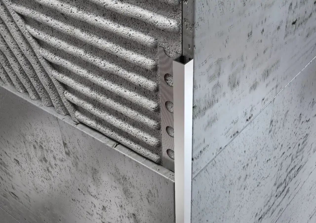 Angolo di un muro con piastrelle grezze e un profilo jolly in alluminio che rifinisce il bordo.