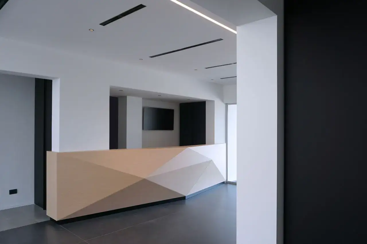 Un moderno bancone reception in cartongesso con pannelli geometrici in legno chiaro, un design accattivante per un ufficio.