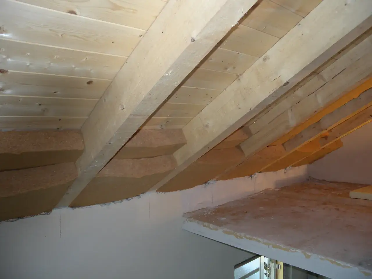 Soffitto a vista con travi in legno e pannelli isolanti in fibra di legno. L'isolamento è posizionato tra le travi per un soffitto a vista efficiente.